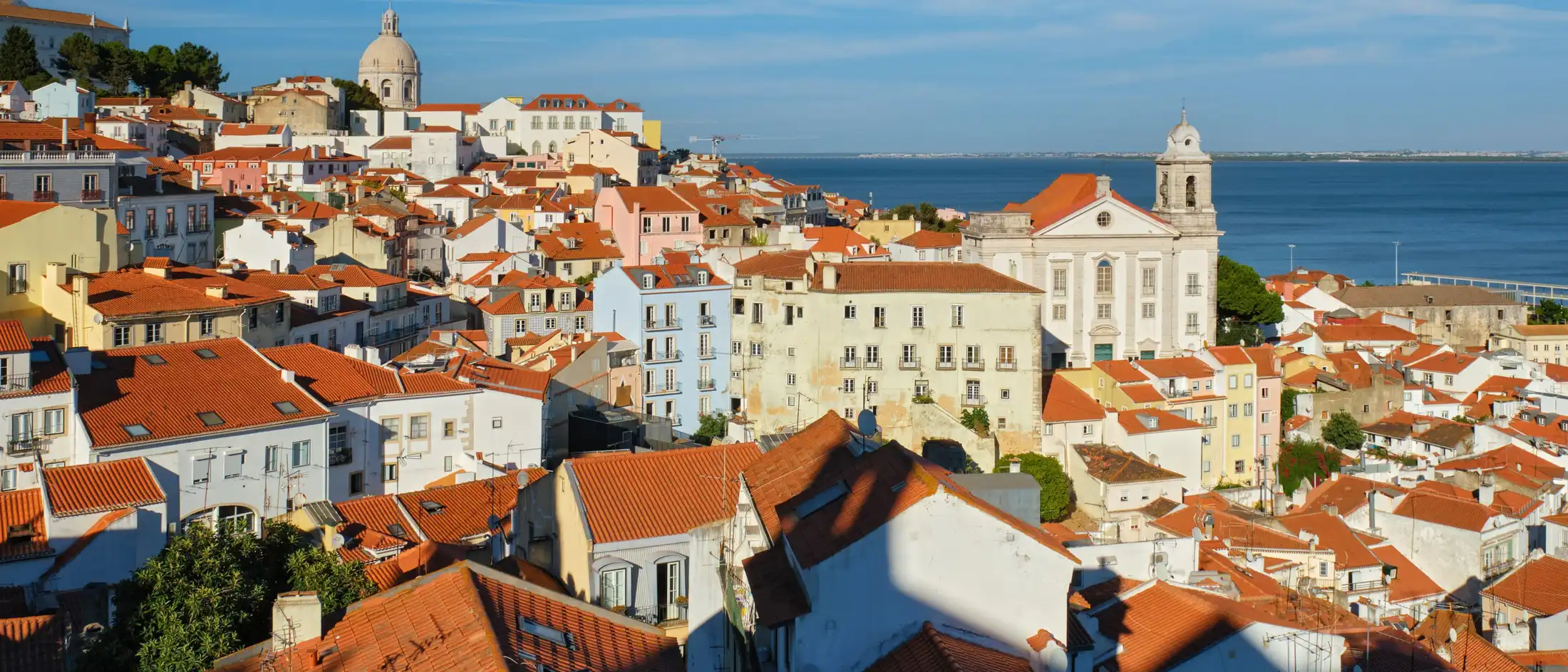Alfama rooftops and the Tagus seen from Miradouro de Santa Luzia in daylight