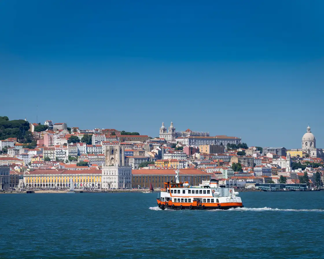 An orange cacilheiro ferry crossing the Tagus with the Lisbon waterfront behind